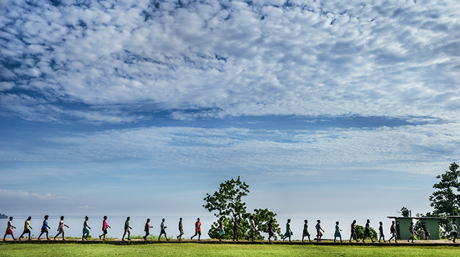 Wide shot of a group of people walking in line formation outside.