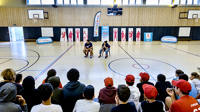 Group discussion with two leaders in a gym filled with kids.