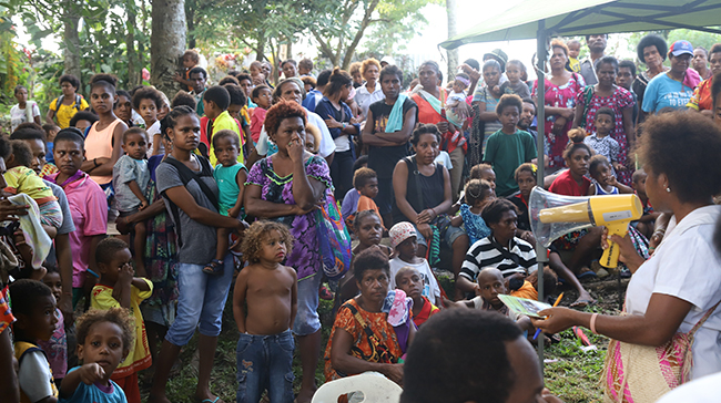 Group of villagers gathered around a speaker with a megaphone.